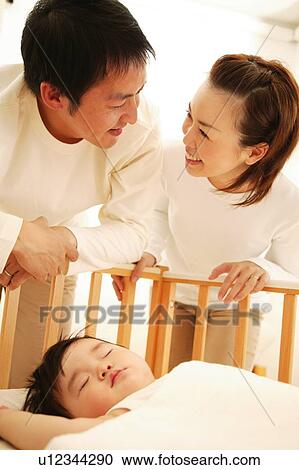 Stock Image - Parents looking at their baby over the baby bed. Fotosearch
