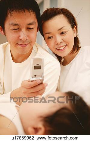 Stock Image - Parents taking a photograph of their baby by mobile phone. Fotosearch