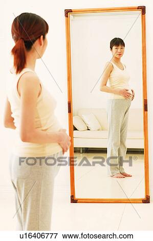 Stock Photo - Pregnant Woman looking herself through the mirror. Fotosearch