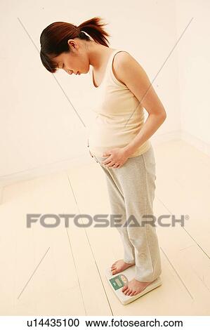Stock Image - Pregnant Woman measuring her weight. Fotosearch
