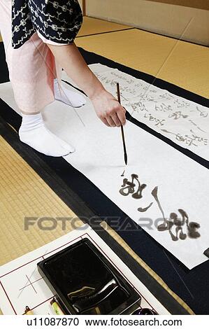 Stock Image - Woman writing charactersin a Japanese paper. Fotosearch