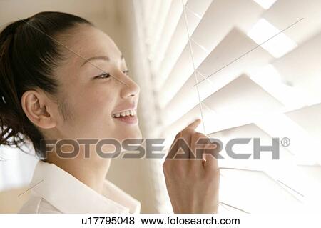 Stock Photo - Young Woman Looking Outside Through Blinds. Fotosearch
