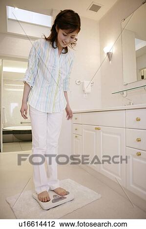 Stock Image - Young Woman Standing On Bathroom Scale. Fotosearch