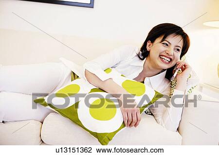 Stock Image - Young Woman Talking On Mobile Phone and Lying Down. Fotosearch