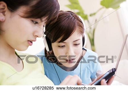 Stock Photography - Young Women Using PDA and Listening Music. Fotosearch