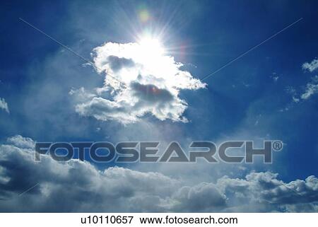 Stock Photo - The sun and clouds in the blue sky, low angle view, lens flare. Fotosearch