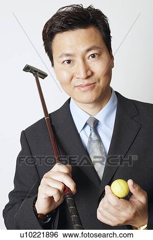 Stock Photograph - Close-up of a businessman holding a golf club and a golf ball. Fotosearch