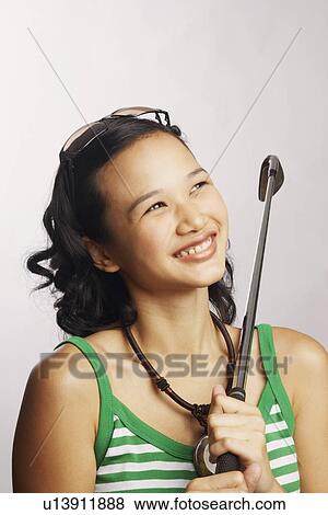 Stock Photo - Close-up of a young woman holding a golf club and looking up. Fotosearch