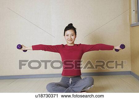 Stock Image - Portrait of a young woman exercising with dumbbells. Fotosearch