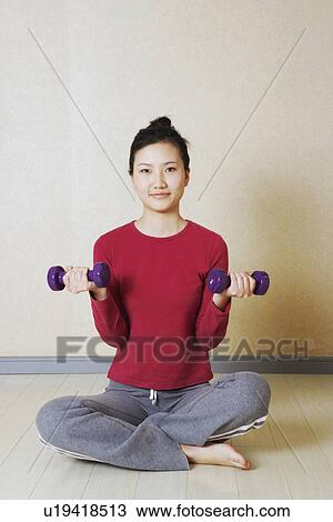 Stock Image - Portrait of a young woman exercising with dumbbells. Fotosearch