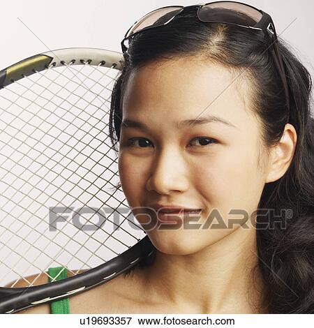 Stock Photo - Portrait of a young woman holding a tennis racket and smiling. Fotosearch