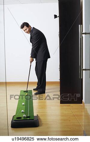 Stock Photography - Side profile of a businessman practicing golf in a club. Fotosearch