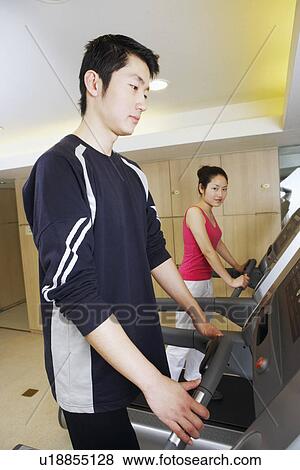 Stock Photo - Side profile of a young man and a young woman exercising in a gym. Fotosearch