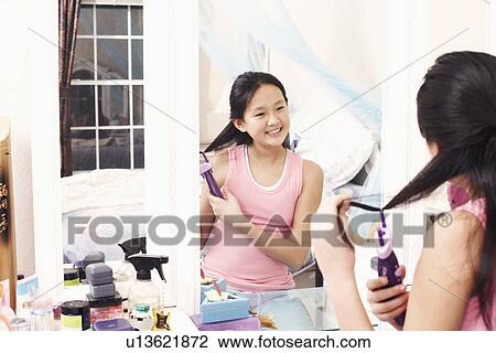 Girl styling her hair in the mirror View Large Photo Image Stock Image - Girl styling her hair in the mirror. Fotosearch