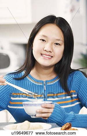 Stock Photo - Portrait of a girl holding a pair of chopsticks and a bowl. Fotosearch