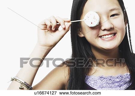 Stock Photo - Portrait of a teenage girl covering her eye with a lollipop. Fotosearch