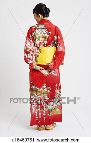 Stock Image - Rear view of a young woman standing and wearing traditional clothing. Fotosearch