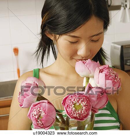 Stock Image - Close-up of a young woman holding a flower vase in the kitchen. Fotosearch