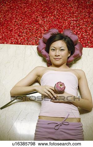 Stock Photo - High angle view of a young woman lying on the floor near a hot tub filled with rose petals. Fotosearch