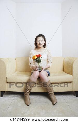 Stock Photo - Portrait of a young woman sitting on a couch holding a flower pot. Fotosearch