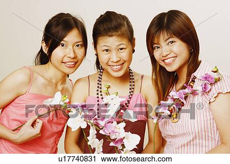 Stock Image - Portrait of three young women holding flowers and smiling. Fotosearch
