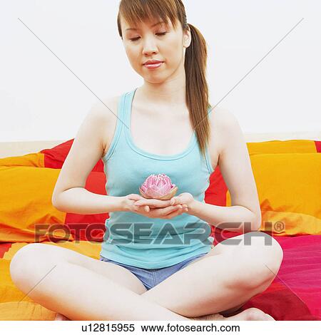 Stock Photography - Young woman holding a lotus flower and meditating on the bed. Fotosearch