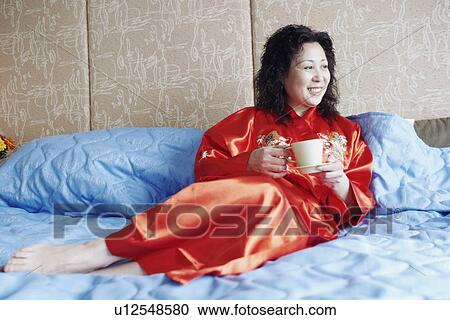 Mature woman lying on the bed holding a cup of tea View Large Photo Image Stock Image - Mature woman lying on the bed holding a cup of tea. Fotosearch