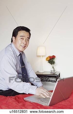 Portrait of a businessman sitting on the bed using a laptop View Large Photo Image Stock Image - Portrait of a businessman sitting on the bed using a laptop. Fotosearch
