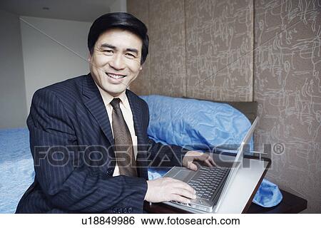 Stock Photograph - Portrait of a businessman sitting on the bed smiling. Fotosearch