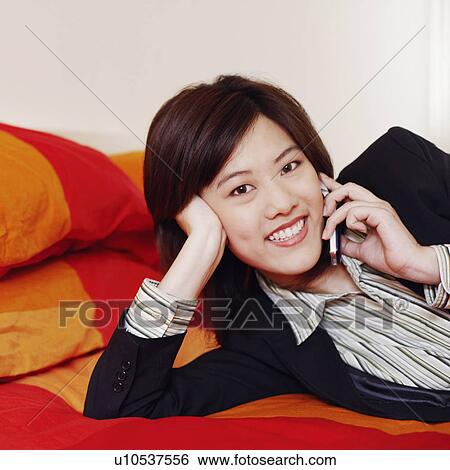 Stock Photograph - Portrait of a businesswoman lying on the bed and talking on a mobile phone. Fotosearch