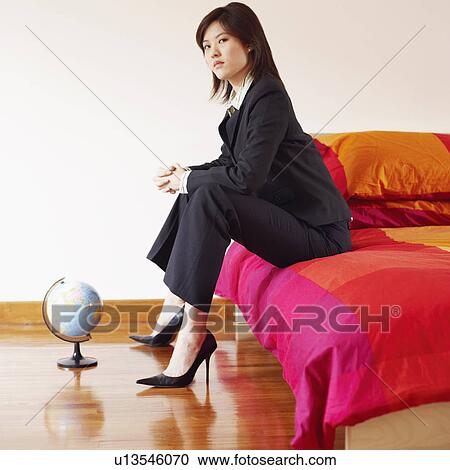 Stock Image - Portrait of a businesswoman sitting on the bed with her hands clasped. Fotosearch