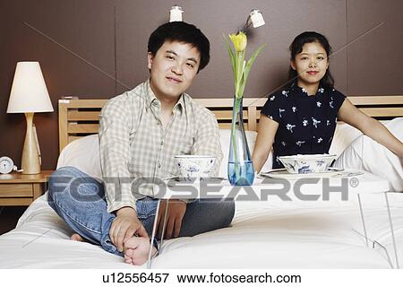 Stock Photo - Portrait of a young man and a mid adult woman sitting on the bed. Fotosearch