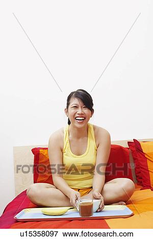 Portrait of a young woman laughing and sitting on the bed View Large Photo Image Stock Photo - Portrait of a young woman laughing and sitting on the bed. Fotosearch