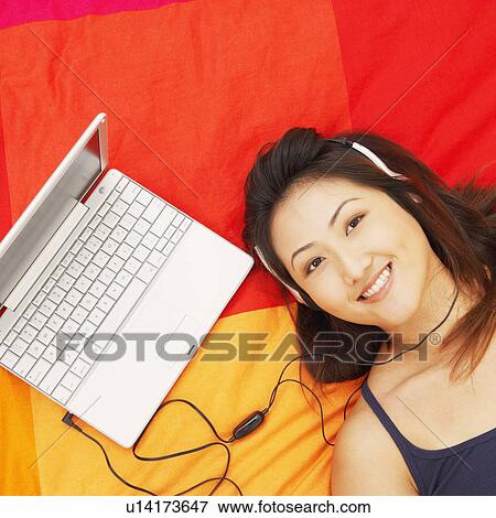 Stock Photo - Portrait of a young woman listening to music on headphones and smiling. Fotosearch