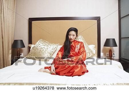 Stock Photo - Portrait of a young woman sitting on the bed. Fotosearch