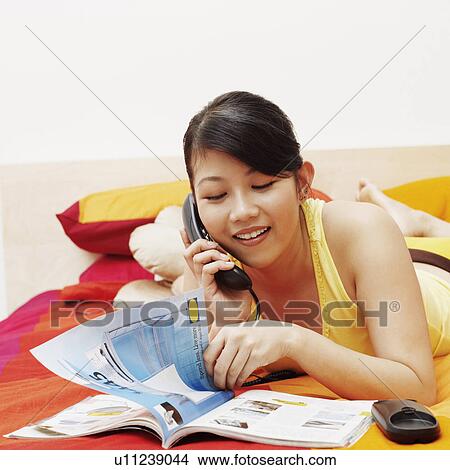 Picture - Young woman talking on the telephone and reading a magazine. Fotosearch