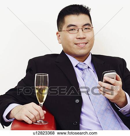 Stock Photo - Portrait of a businessman holding a champagne flute and a mobile phone. Fotosearch