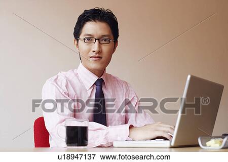 Portrait of a businessman sitting in an office and using a laptop View Large Photo Image Stock Photo - Portrait of a businessman sitting in an office and using a laptop. Fotosearch