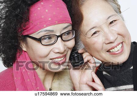 Stock Photo - Portrait of a mature woman with her friends using a mobile phone. Fotosearch