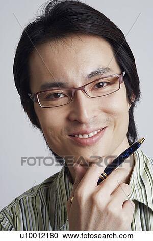 Stock Image - Portrait of a mid adult man holding a pen with his hand on his chin. Fotosearch