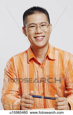 Stock Image - Portrait of a mid adult man holding a pen and smiling. Fotosearch