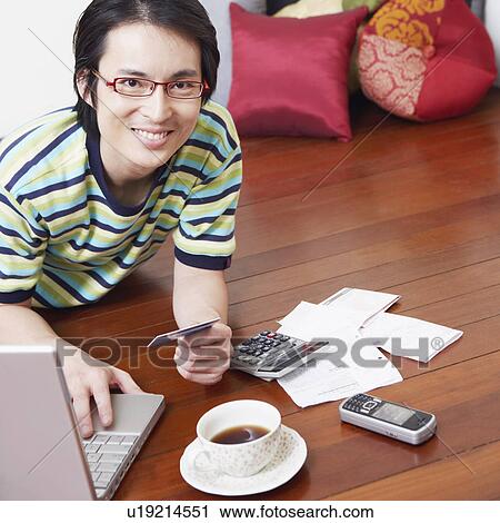 Stock Image - Portrait of a mid adult man using a laptop and holding a credit card. Fotosearch