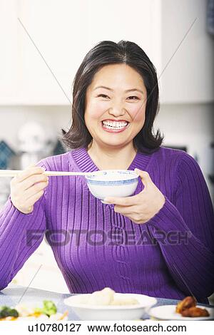 Stock Photo - Portrait of a mature woman holding a bowl with a pair of chopsticks. Fotosearch