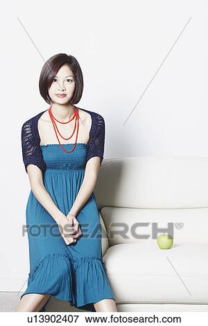Stock Photo - Portrait of a young woman sitting on the arm of an arm chair. Fotosearch