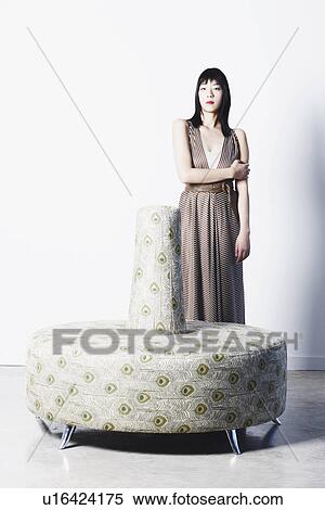 Stock Photography - Portrait of a young woman standing behind a couch. Fotosearch