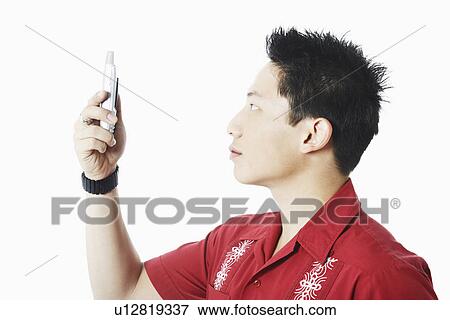 Stock Photo - Side profile of a young man holding a mobile phone. Fotosearch
