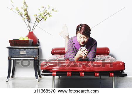 Stock Image - Young woman lying on the bed holding a mobile phone. Fotosearch