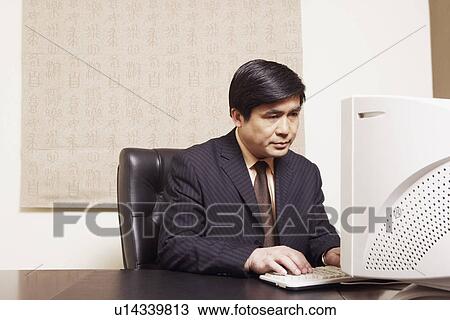 Businessman sitting in an office using a computer View Large Photo Image Stock Image - Businessman sitting in an office using a computer. Fotosearch