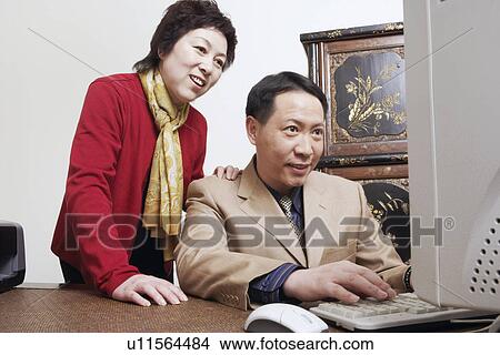 Picture - Businessmen using a computer with a businesswomen standing behind her. Fotosearch
