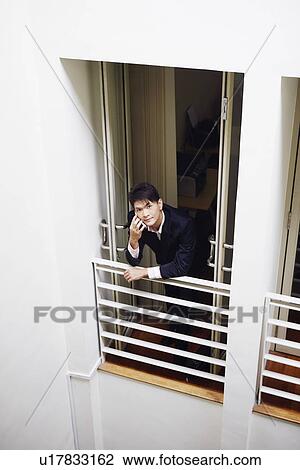 Stock Image - High angle view of a businessman standing at the doorway in an office and talking on a mobile phone. Fotosearch
